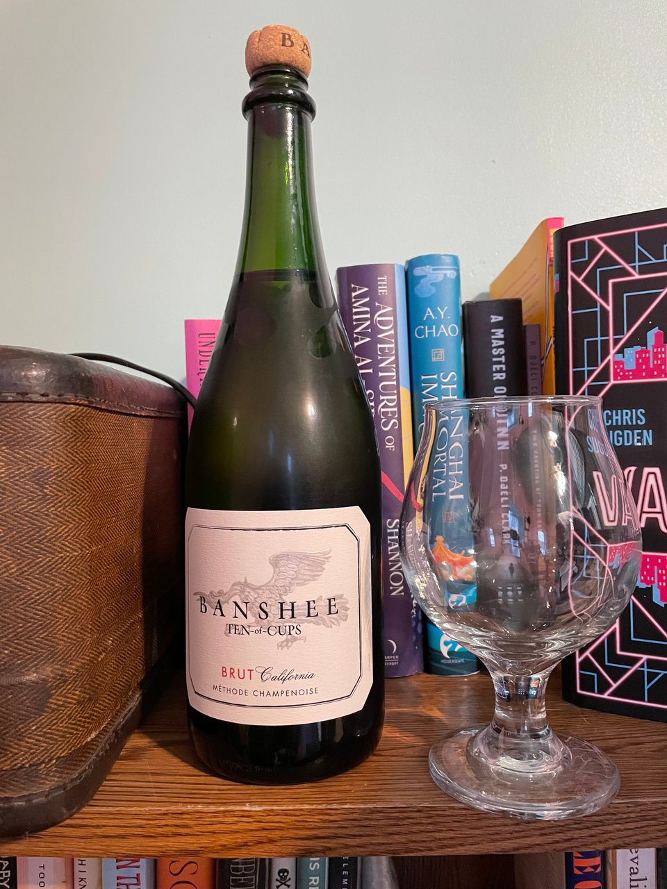 A bottle of Banshee prosecco next to an empty glass, in front of some amazing books.