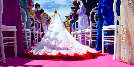 Another Simple Favor still. Blake Lively's character walks down the aisle in a wedding dress with a train that has bloodred edges.