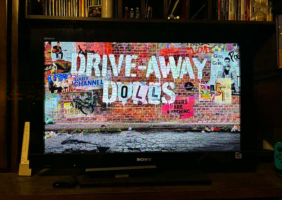 A photo of my TV, from when I was watching Drive-Away Dolls, specifically of when the title came on screen. It looks like graffiti, painted on a brick wall.