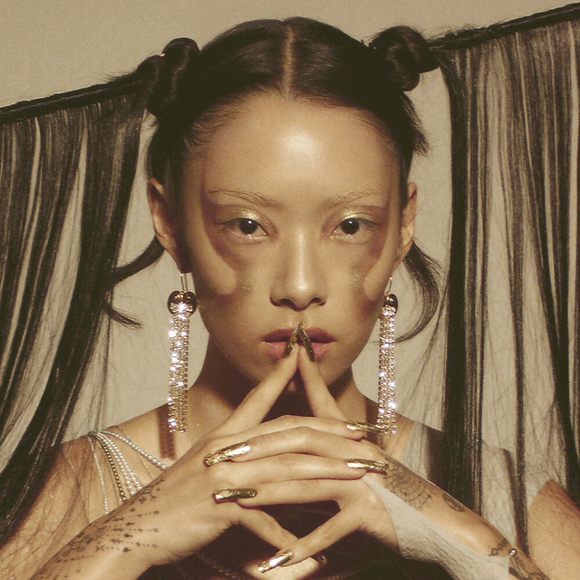 image of Rina Sawayama, a Japanese-British singer wearing sparkling jewelry, sparkling nail polish, sparkling makeup, and their hair drawn up