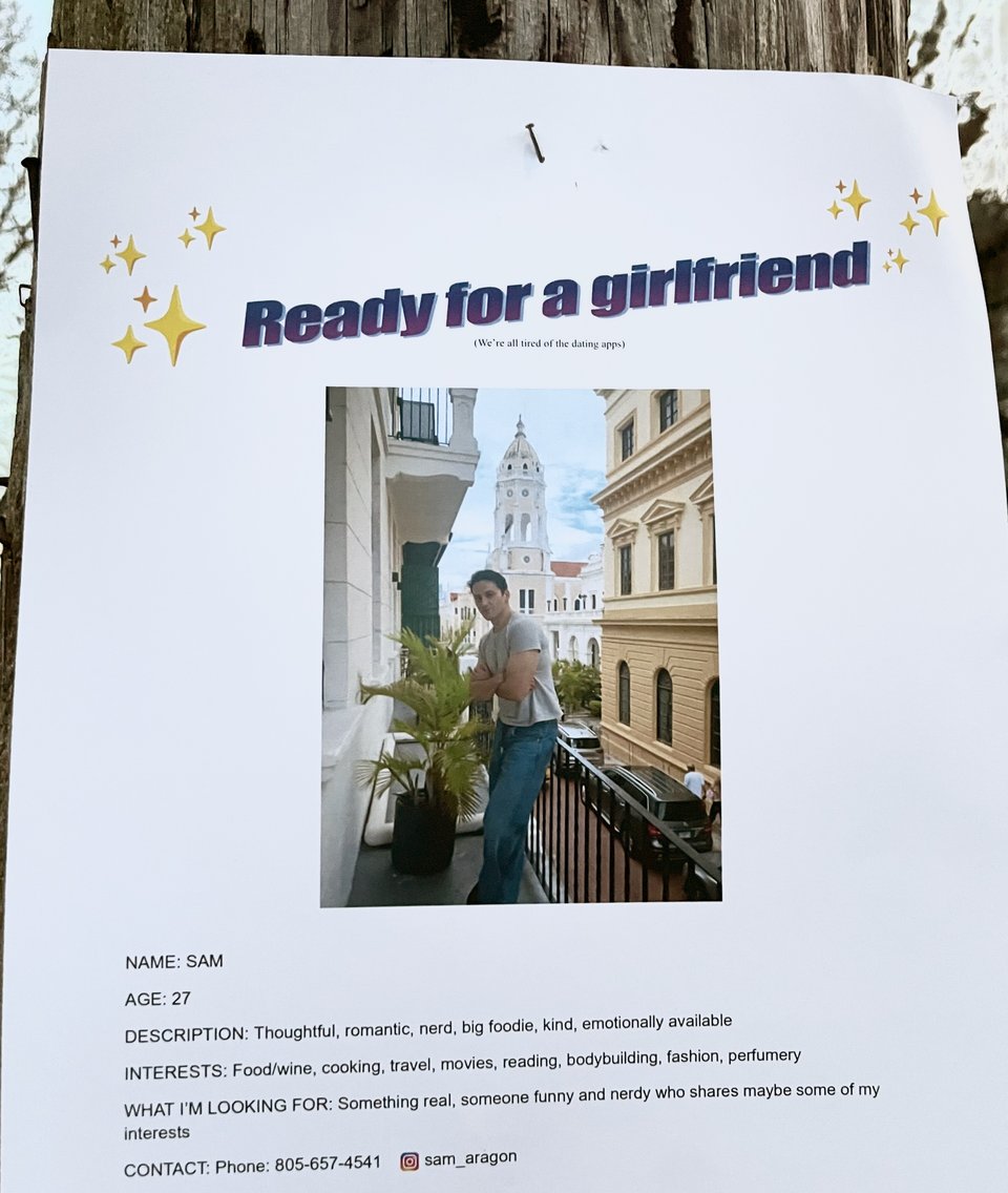 a flyer posted on a telephone by Sam that reads "ready for a girlfriend" with a photo of him