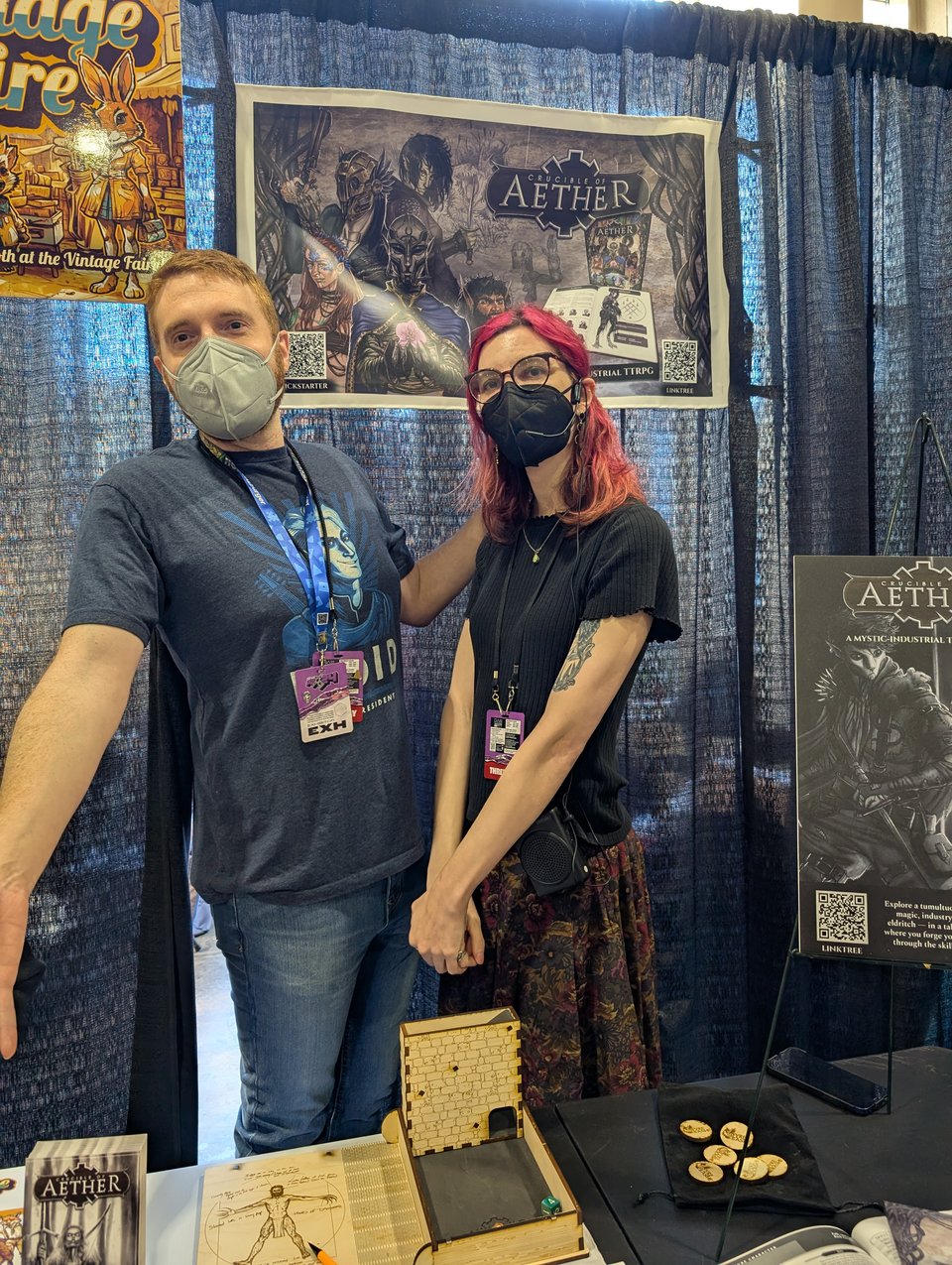 Two of the designers for Crucible of Aether pose at the booth for their game at PAX Unplugged