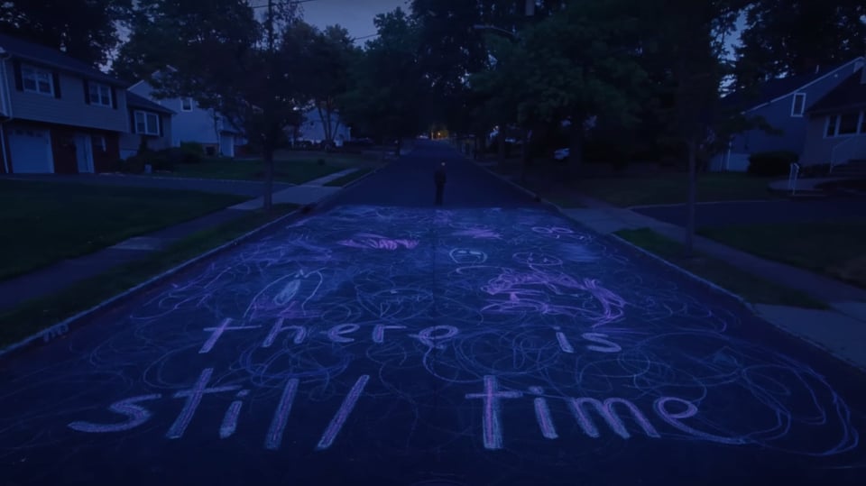 A still from the film I Saw The TV Glow. It's a street with "there is still time" chalked into it.