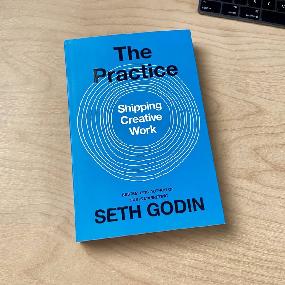 Seth Godin’s book “The Practice” on a wooden desk