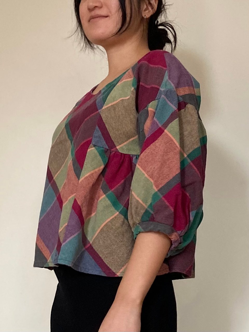 Josephine is wearing a handmade 3/4 length sleeve top with balloon sleeves. The fabric is a plaid pattern with purple, green and yellow