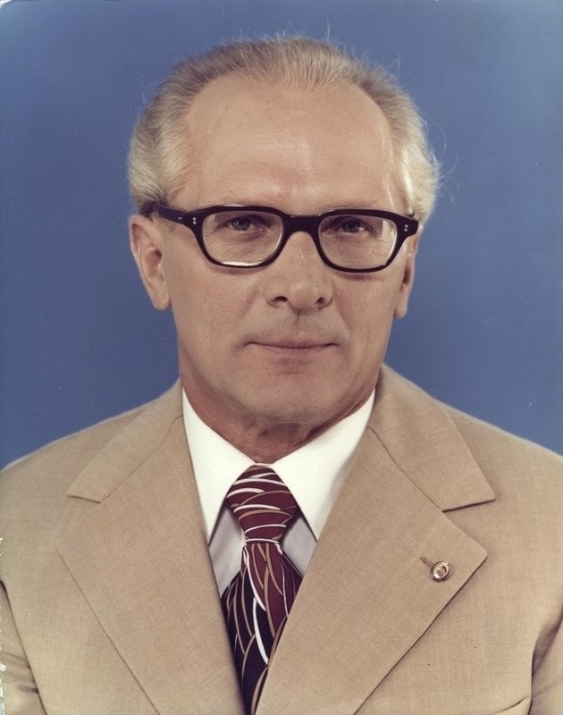 Porträtfoto eines freundlich drein schauenden älteren Herren in heller Anzugjacke vor blauem Hintergrund.