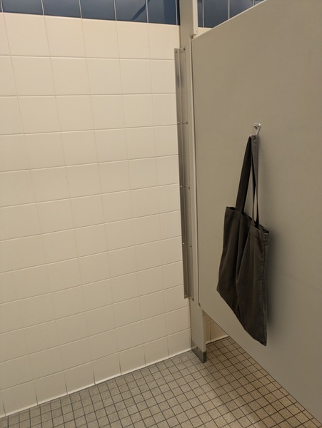 the view from inside a bathroom stall with a tote bag hanging on a hook on the door