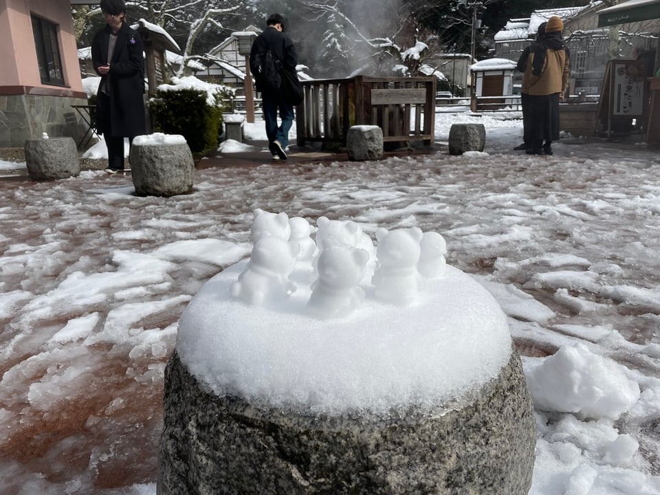 A collection of about 8 mini snowmen the height of two fists mounted on a round stone seat in the middle of town.