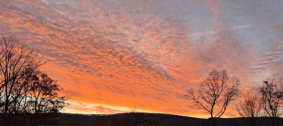 photo of sunrise behind hills with pink/gold/orange clouds spreading across sky