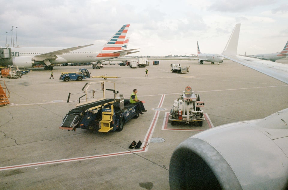 a man sits on a vehicle on the runway, holding the orange guide sticks and kicking his legs out