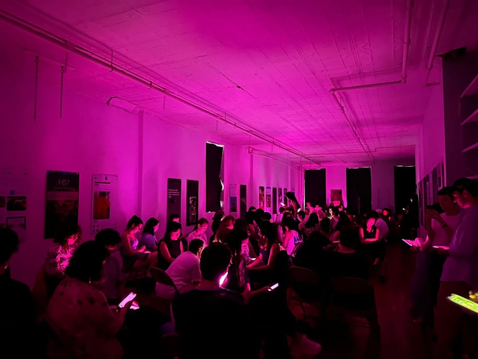 A room of people looking at their phones, which are all glowing fuchsia, such that the entire room is glowing fuchsia.