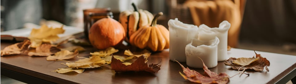 Small gourds, fall leaves, candles, and a book on a table