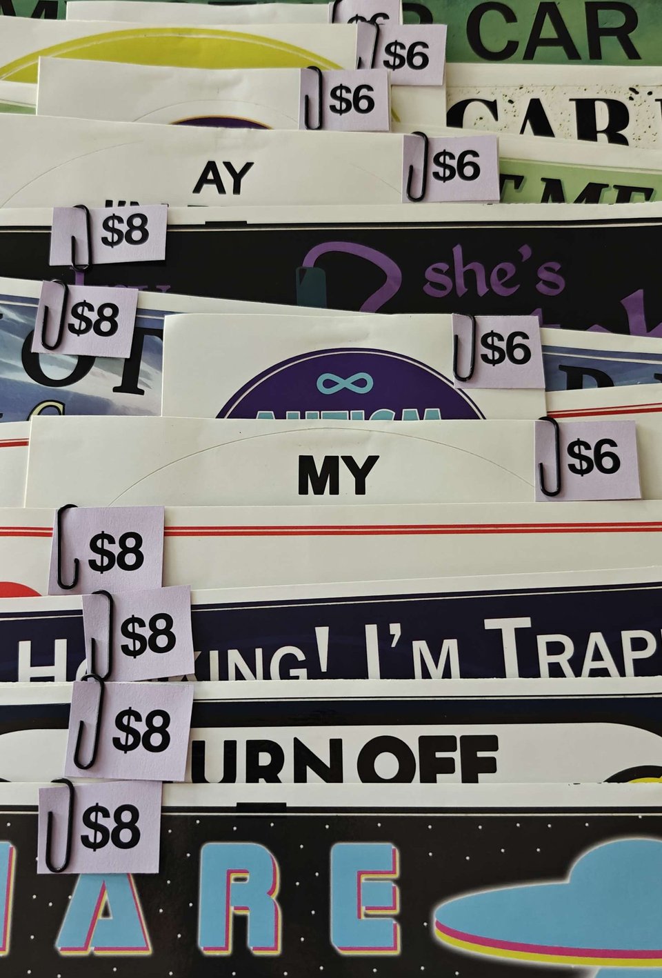 Rows of a.c.d works bumper stickers with price tags denoting $8 or $6 paper clipped to them