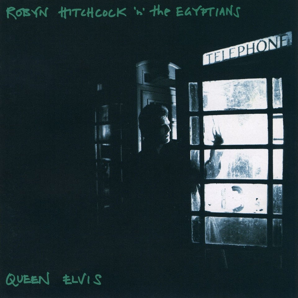 A blue-tinted black and white photograph of Robyn Hitchcock stepping out of a telephone booth. The only source of light is from the booth, everything around is dark. There is a bit of a haunted vibe.