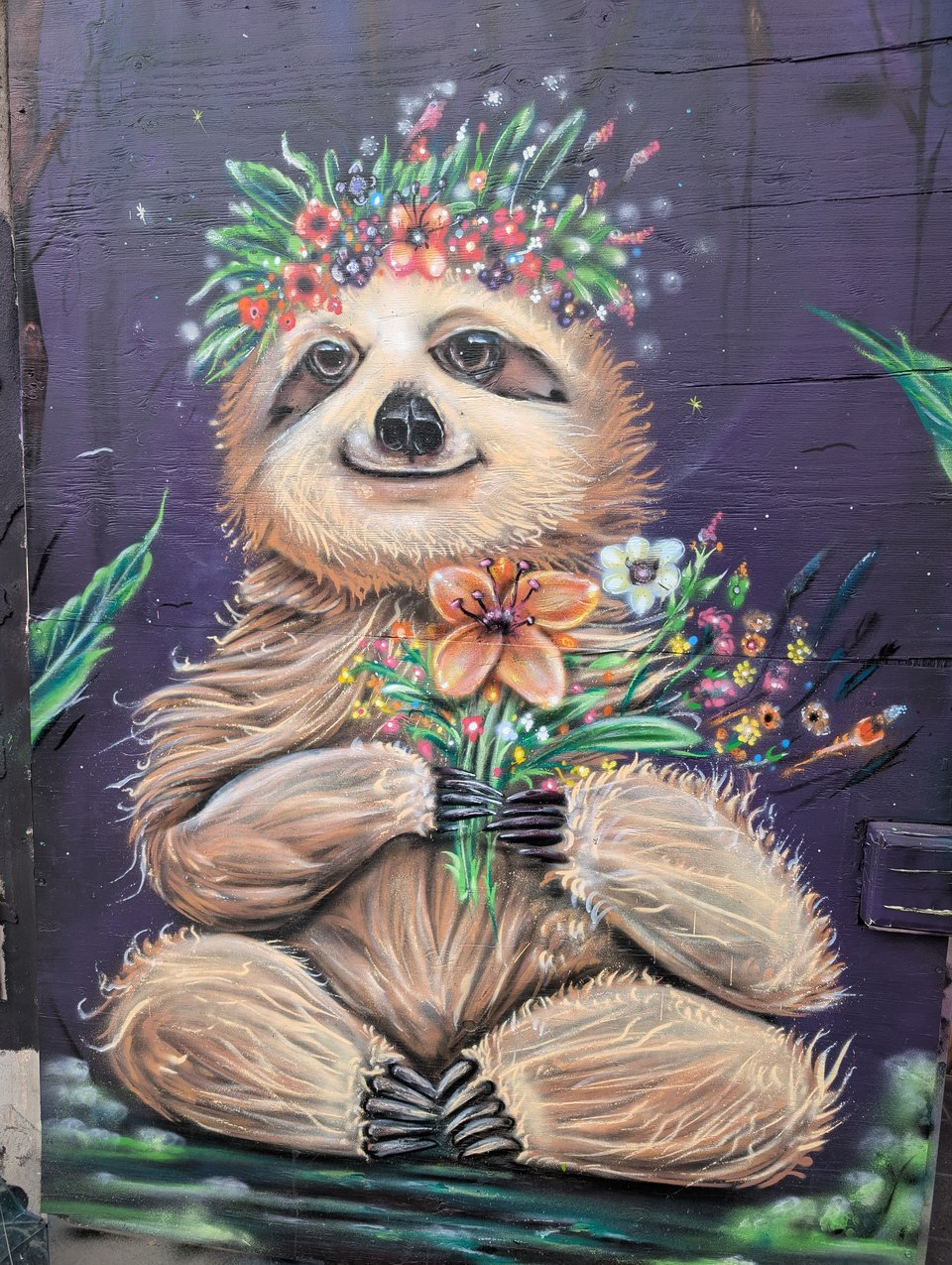 A painting on a wall of a sloth wearing a flower crown and holding a bouquet of flowers.