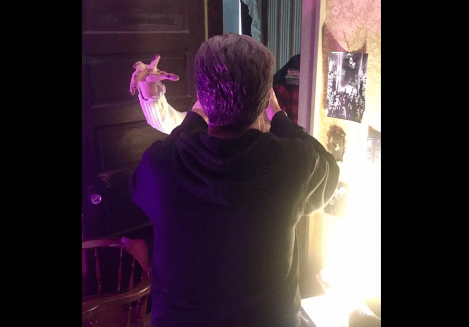 The back of a man's head as he holds a camera, a monster's hand reaching around