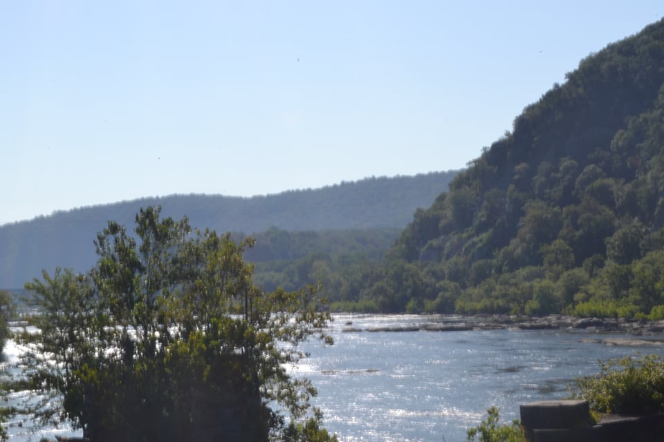 A wide river seen from a bridge. The far bank is steep and wooded.