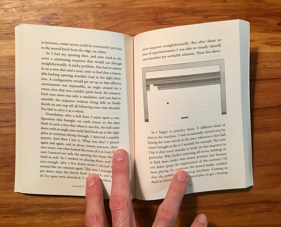 The book "Breakout: Pilgrim in the Microworld" opened by a hand and showing two pages.