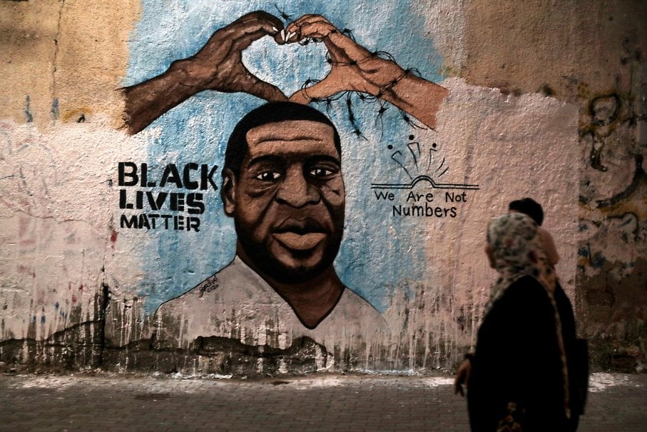 a mural of George Floyd that says "BLACK LIVES MATTER" and "We Are Not Numbers." Three people in the foreground, one of whom is a hijabi.