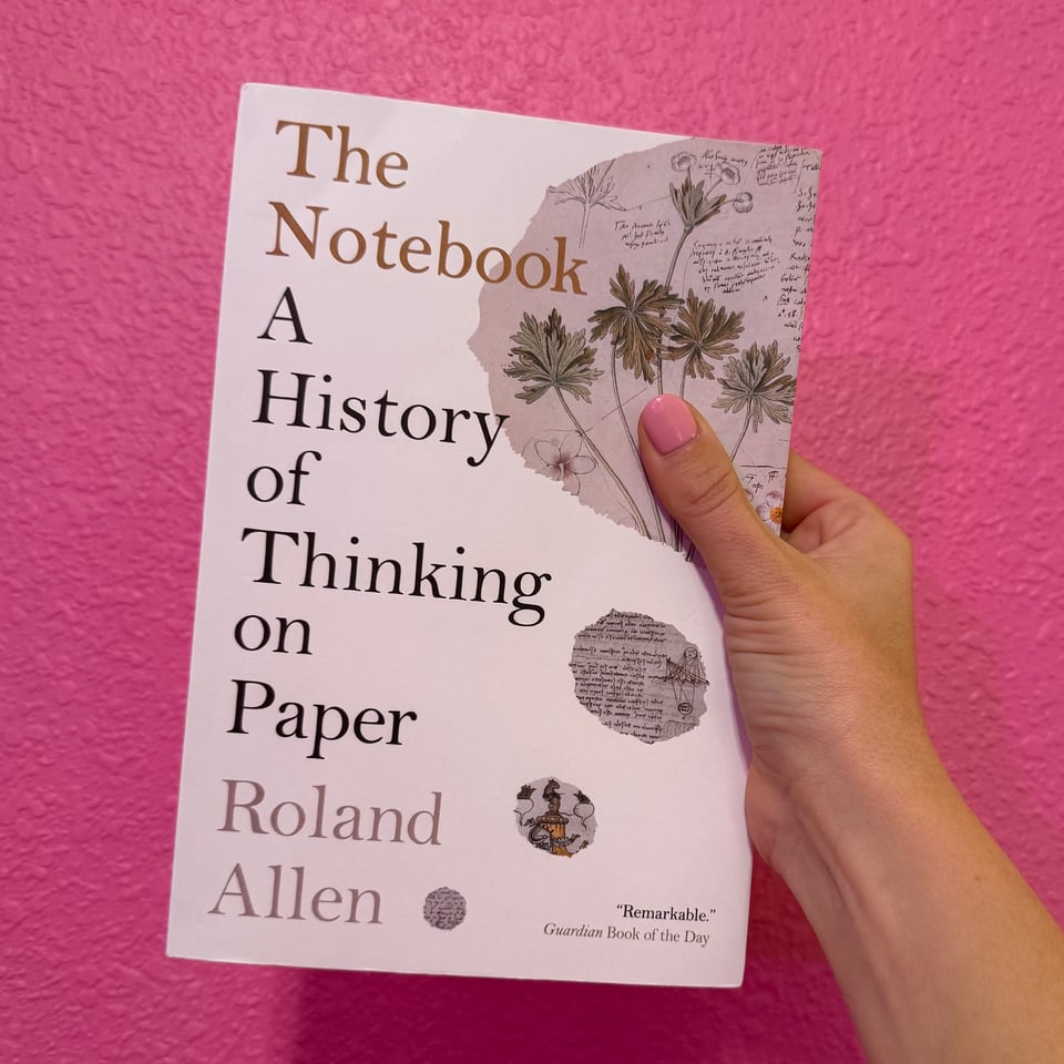 Me holding the book, The Notebook: a history of thinking on paper by Rolan Allen, against a pink background.