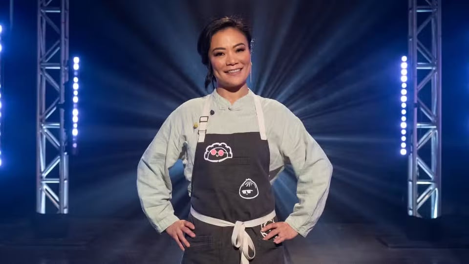 A person in a chef's coat smiling and posing in front of dramatic lights