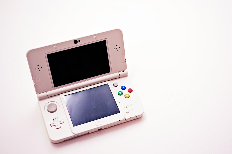 Stock photo of a pink nintendo ds sitting on a similarly pink surface.