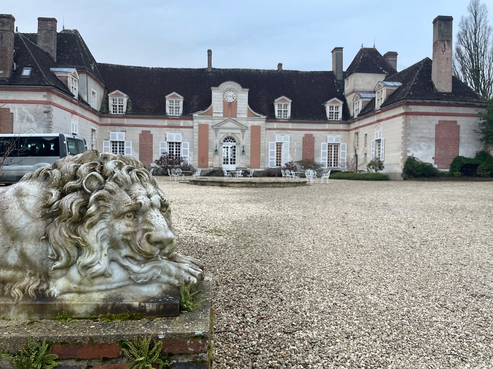 The front of a chateau with a statue of a lion in the foreground.