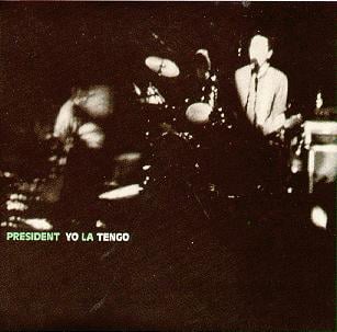 A black and white still of Yo La Tengo in concert, showing a white guy playing guitar and a woman on drums, but the still is, I think, being warped and burned as if caught in a projector. I think. I could not find a good, large version of this picture, so I'm working from a very small one, and my 53 year old eyes can only do so much.