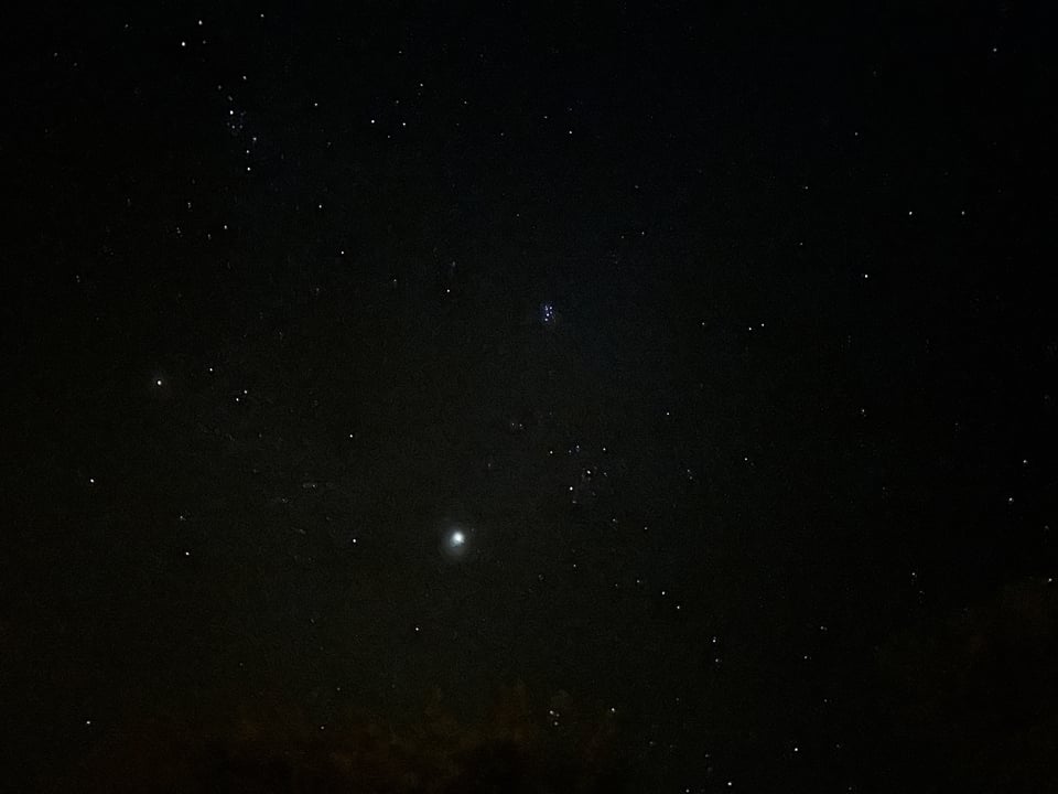 A view of the deep, dark night sky, dozens of small stars (and one larger one) on a background of velvety black