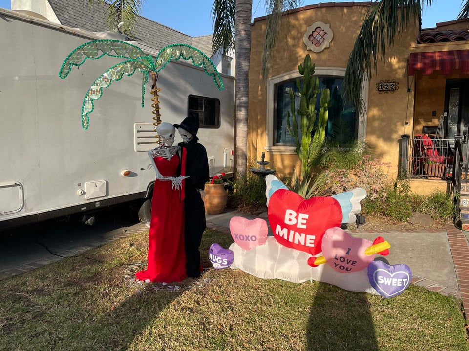 A lawn display. Two skeletons hold one another surrounded by Valentines Day decorations and LA sunshine