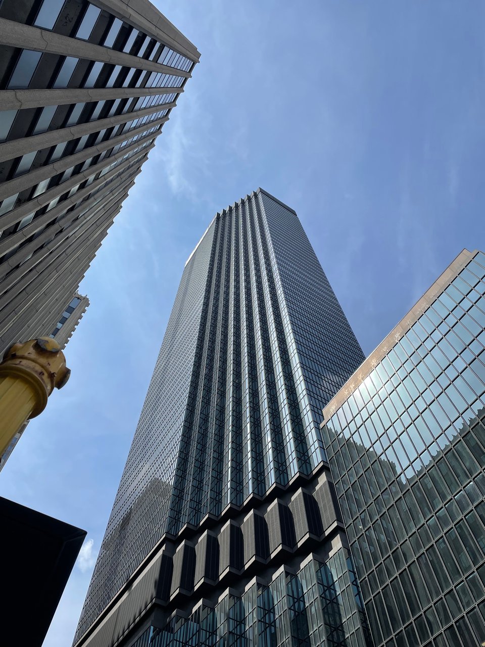 A tall blue skyscraper seen from the ground, soaring into blue skies
