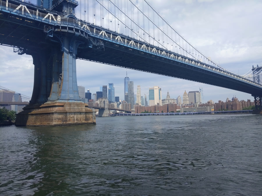 Photograh of the Manhattan Bridge over the East River taken from DUMBO. The Manhattan Skyline can be seen under the Manhattan Bridge from this angle.