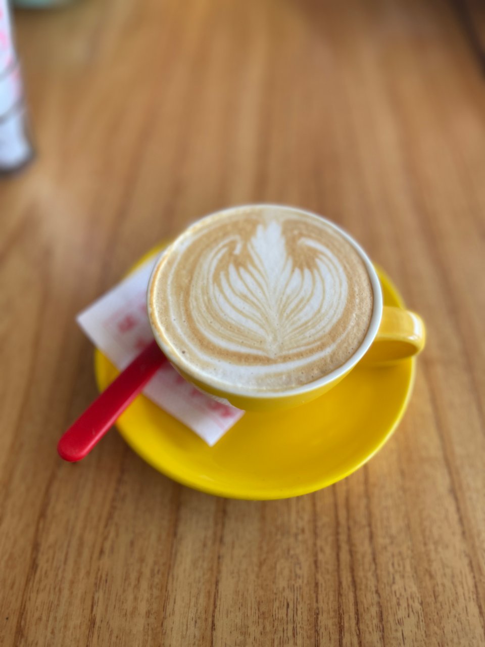 Cappuccino in a bright yellow cup and saucer on a wooden table.