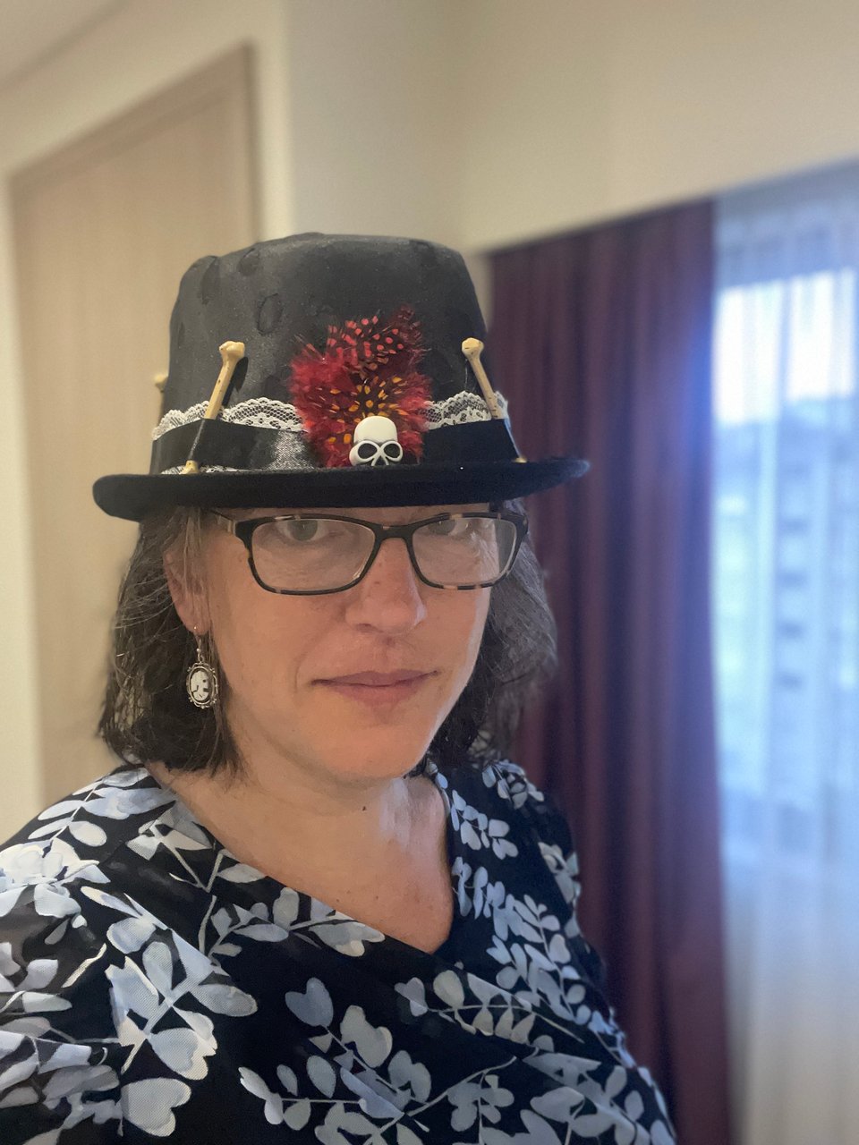 A woman wears a hat and earrings with Day of the Dead theme.