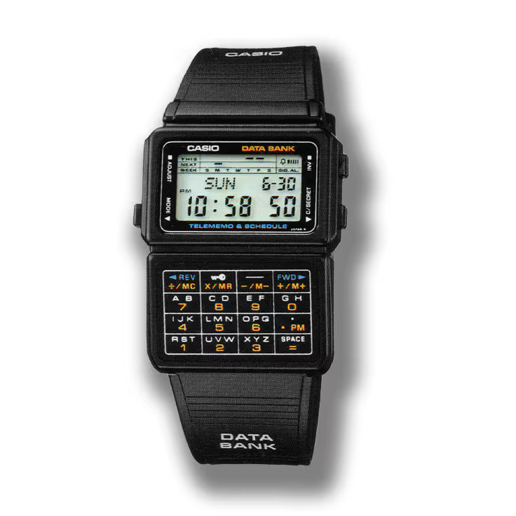 A retro Casio Data Bank digital watch is shown with its rectangular display and a full alphanumeric keypad beneath the screen. The display shows the day, date, and time, while the buttons on the keypad are labeled with letters, numbers, and small orange function keys. Its black wristband and compact design highlight the vintage, gadget-forward aesthetic of early digital watches