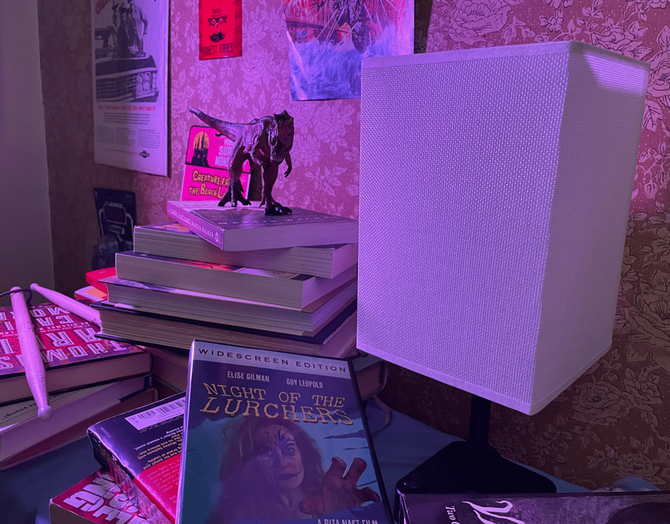 A pile of books, DVDs, and posters with a T-Rex roaring on the top