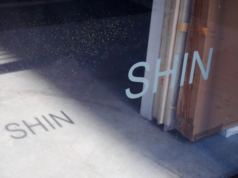 a "Shin" sign in a window, cast upon a concrete floor by the sun.