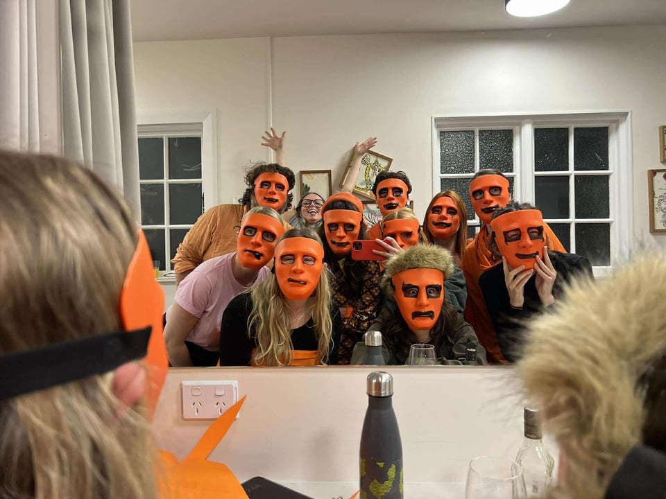The cast of Airhorn taking a selfie in the greenroom, all wearing orange masks with marked on faces
