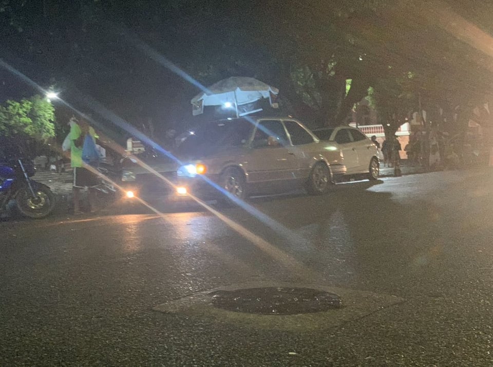 A blurry photo of a car with its headlights on, taken at nighttime on the street with a broken phone.