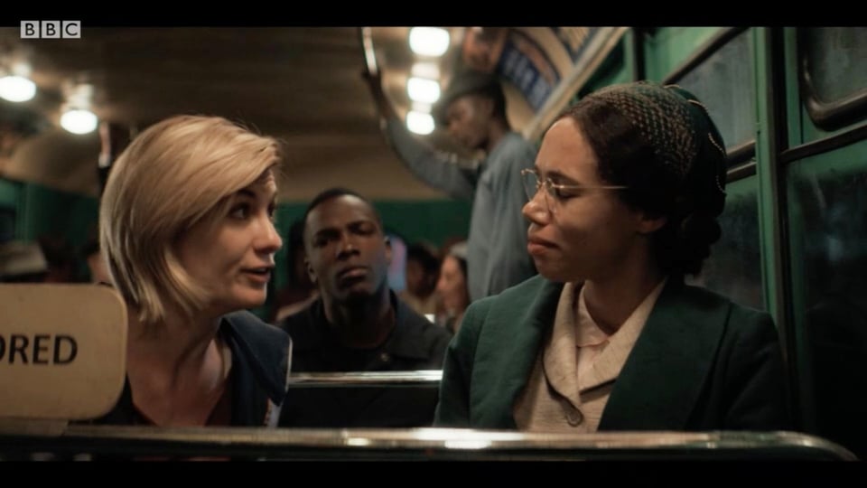 The Doctor sitting next to Rosa Parks on a bus, Ryan sitting behind them.