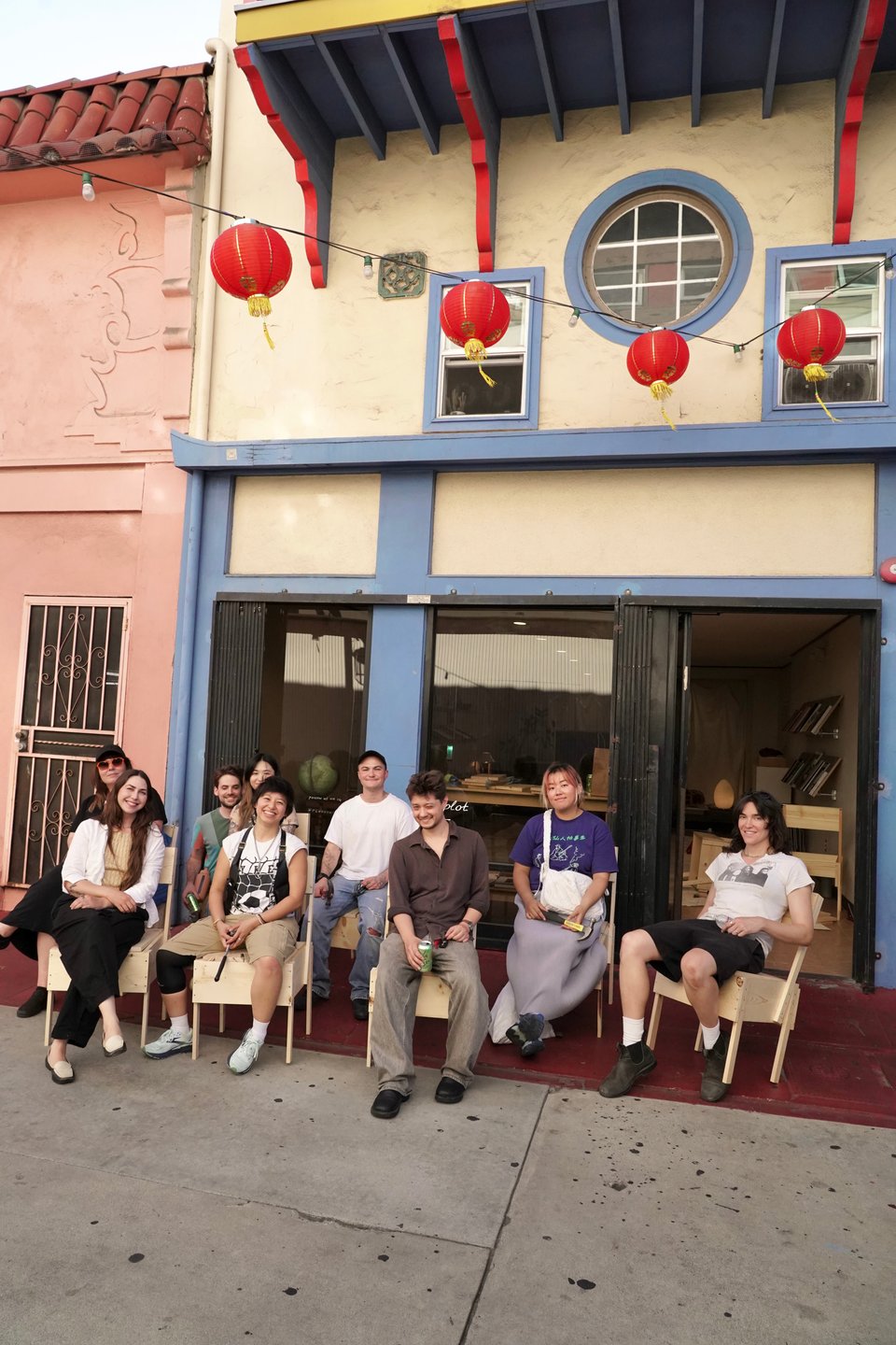 Nine people on wooden chairs in front of the storefront window.