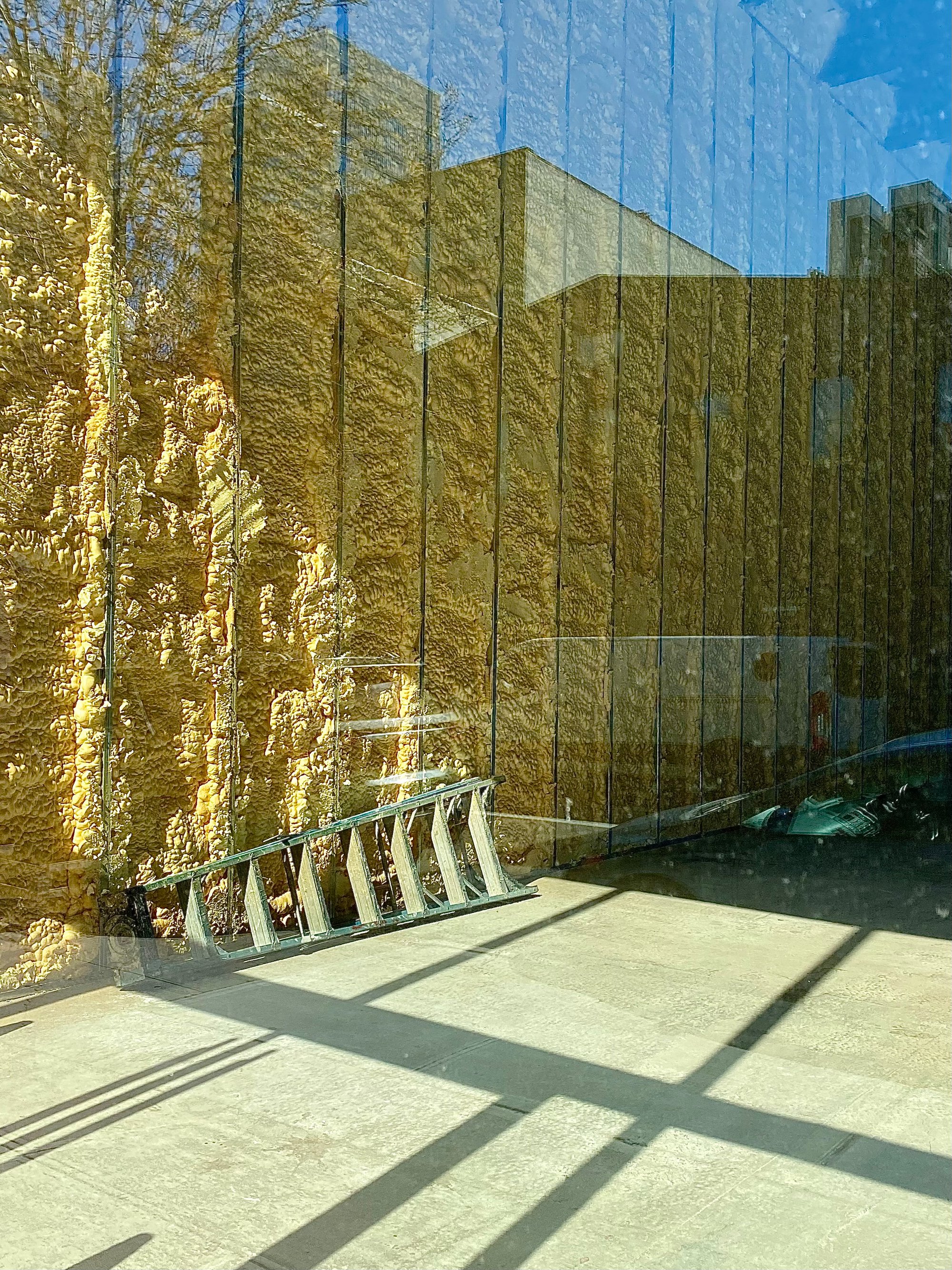 Image of the inside of a building with a ladder on the floor and the reflection of the buildings