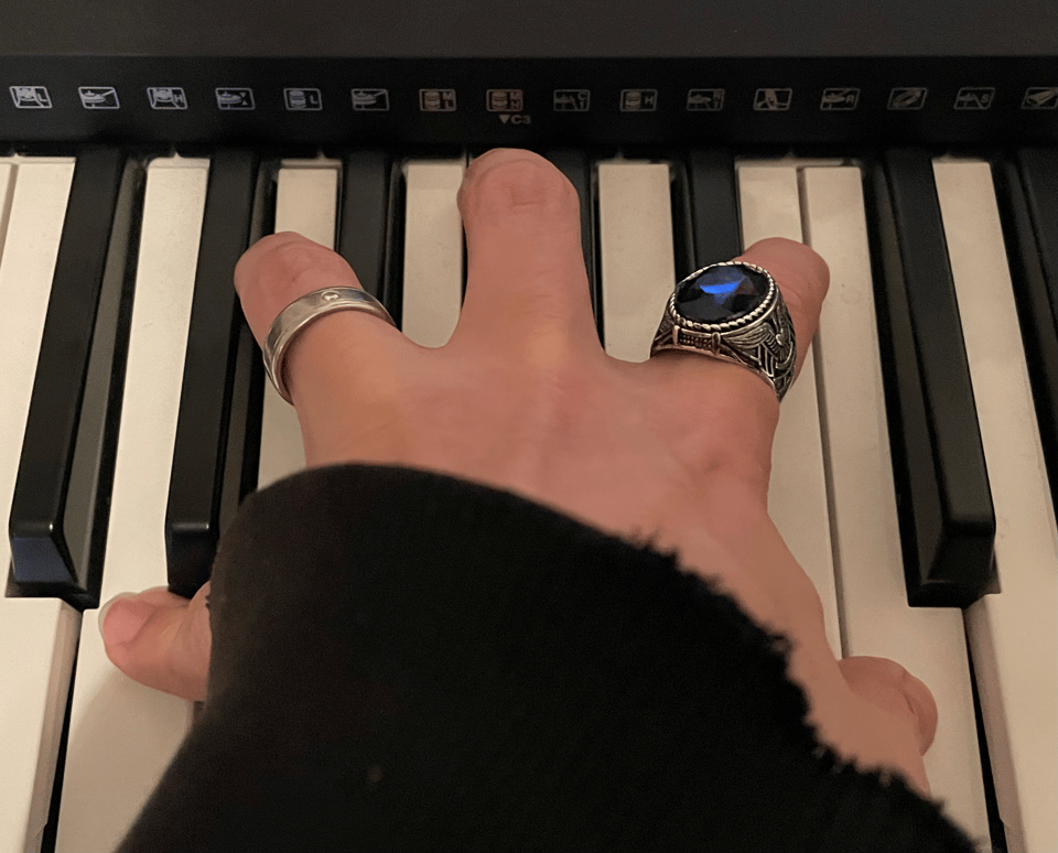 A hand with rings and a tattered black hoodie sleeve pressing down on piano keys