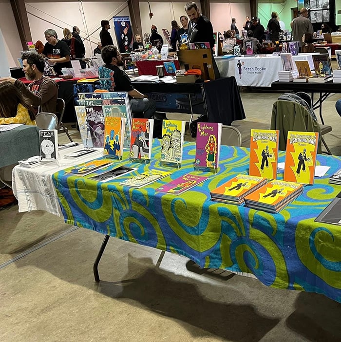 A fuller view of my table at SPACE, with various comics displayed on it, including the individual issues of Lightning Man #1-4.