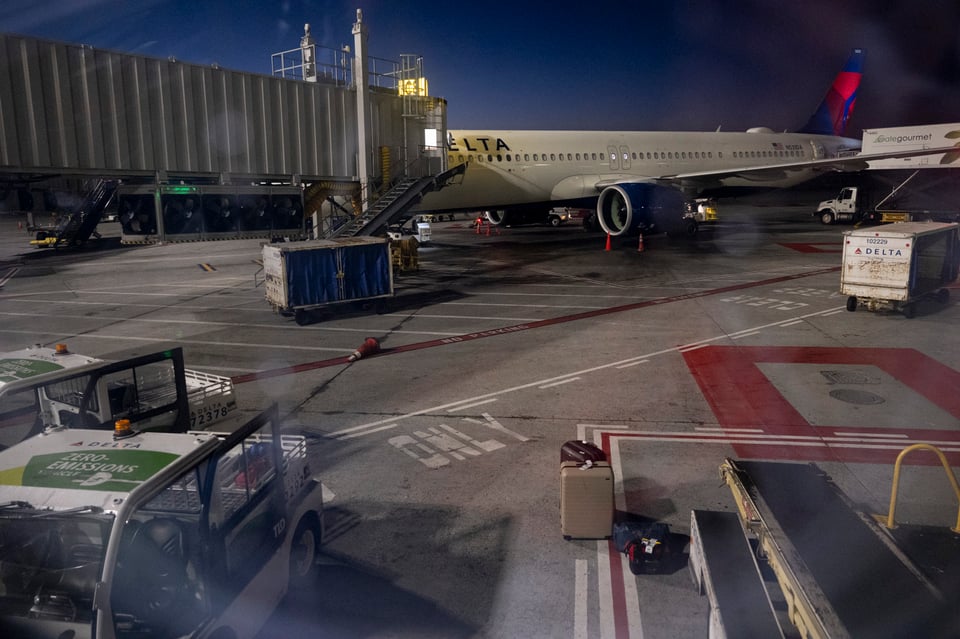 An image of the SFO tarmac out of a plane window, as baggage is being loaded.