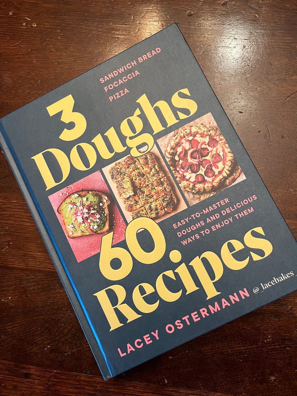 Lacey Osterman's book 3 Doughs 60 Recipes, dark green, on a dark wooden tabletop