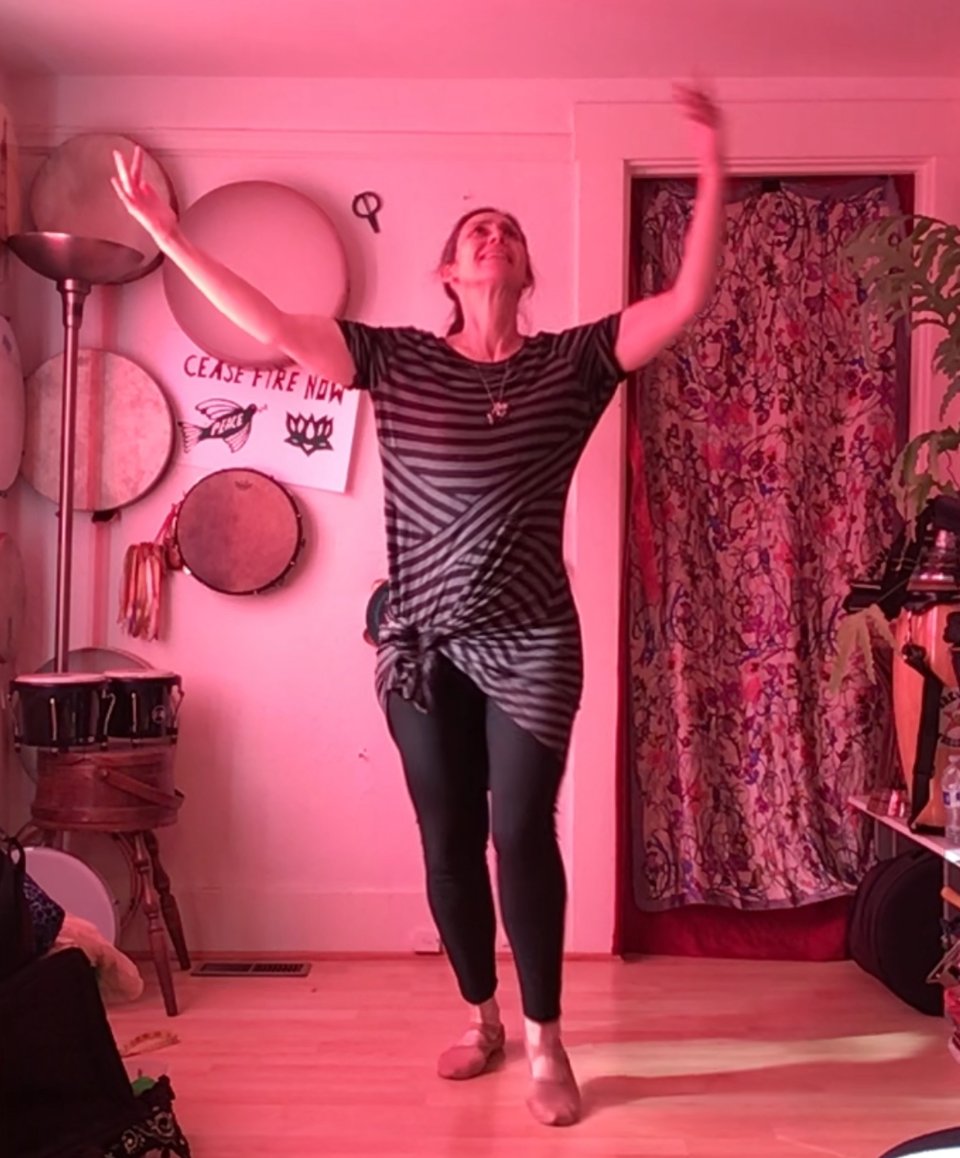 A person looks up, smiling, arms in the air in a grey and black striped dress in a red-lit room