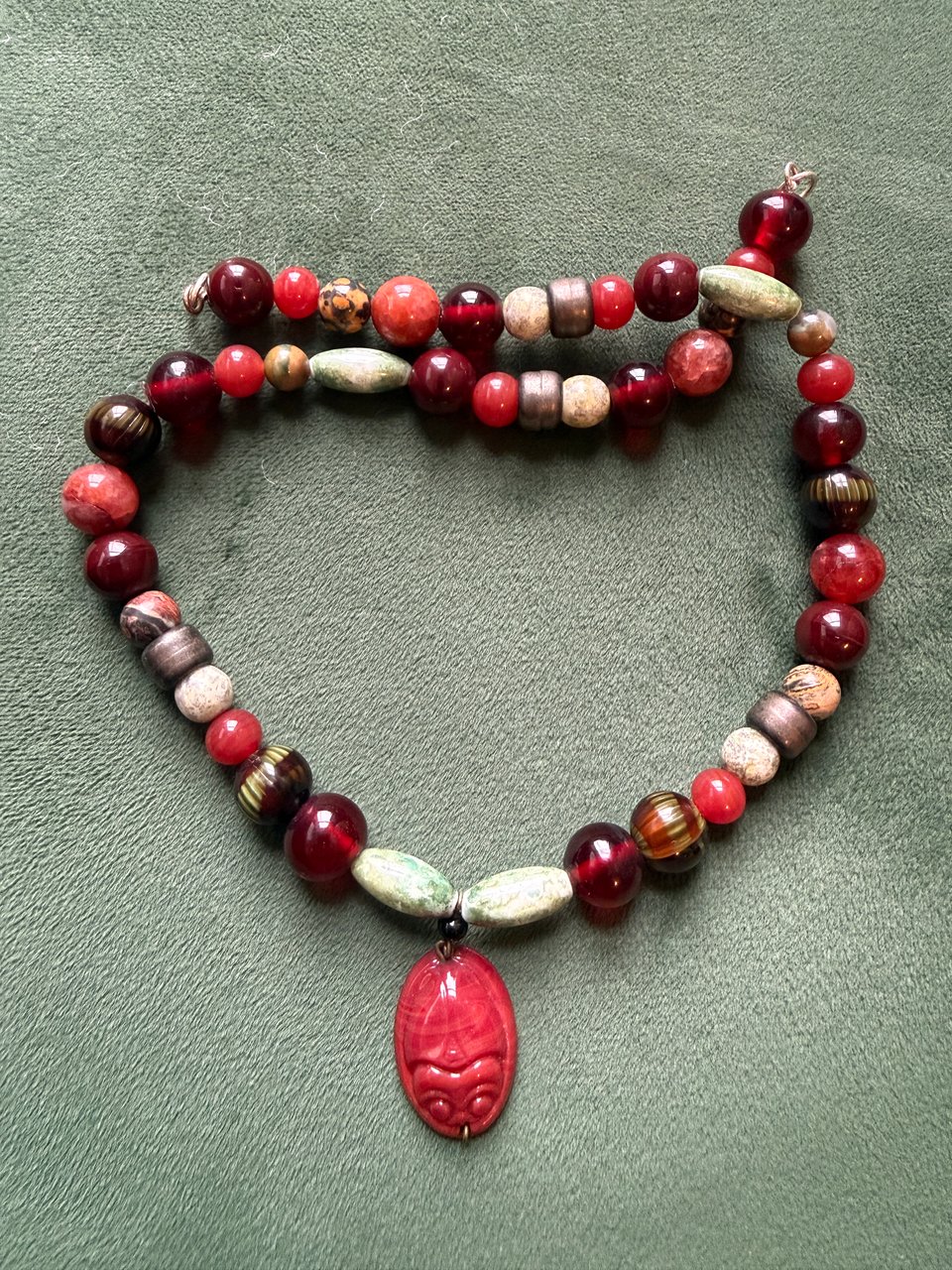 beaded necklace with red scarab pendant and green, red, and earth tone beads against green backdrop
