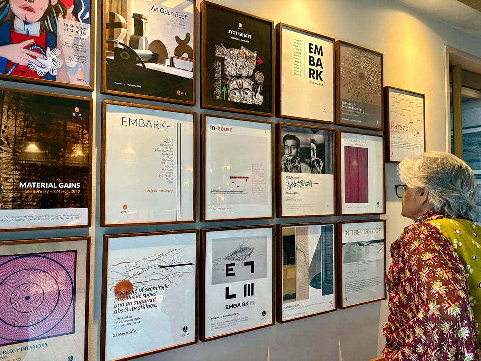 Maya Sharma looking at a set of picture frames on the wall comprising a range of events and exhibitions.