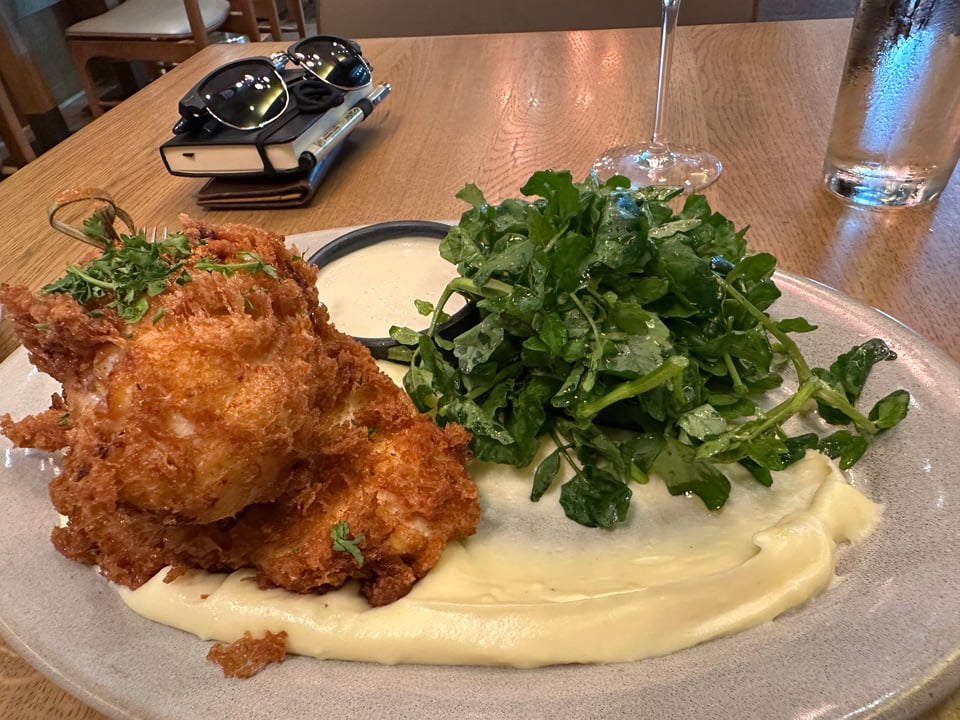 photo of fried chicke atop mashed potatoes & salad on a table, with a pair of sunglasses & sketchpad in the background